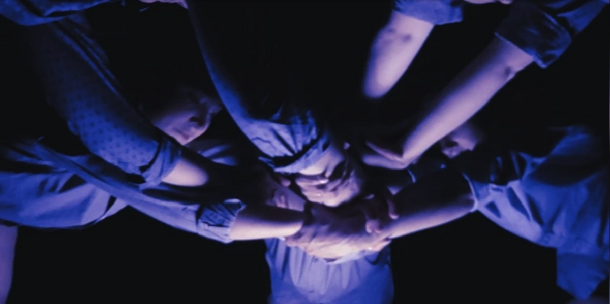 Close-up of hands and faces in a blue wash light